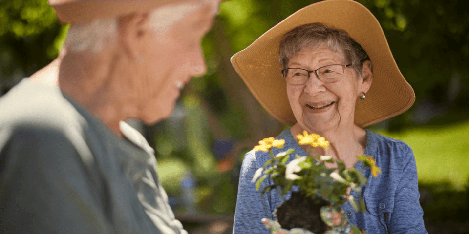 An older woman smiling and holding a plant out toward her friend